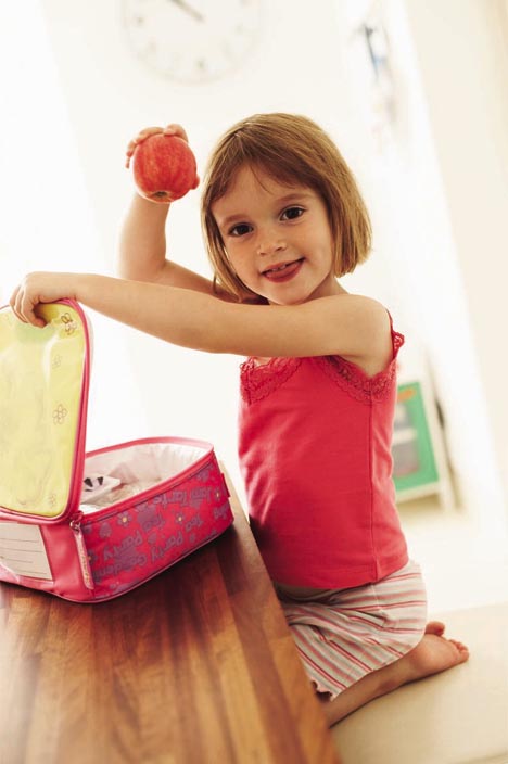 MODEL RELEASED. Packed lunch. Girl holding up an apple from her lunchbox. She is four years old.
